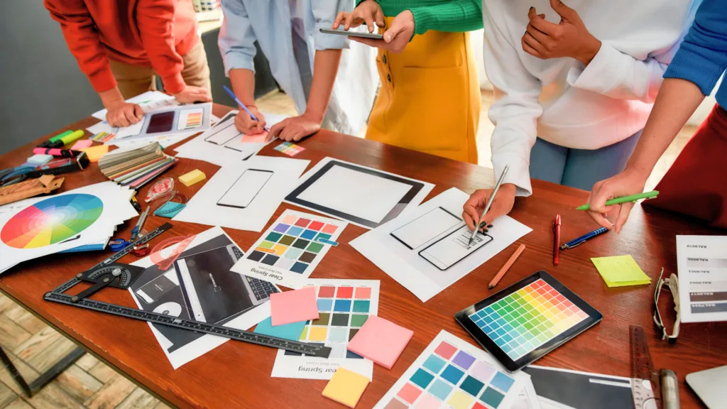 Équipe collaborant sur le design d’une interface web, avec des croquis, palettes de couleurs et prototypes sur une table